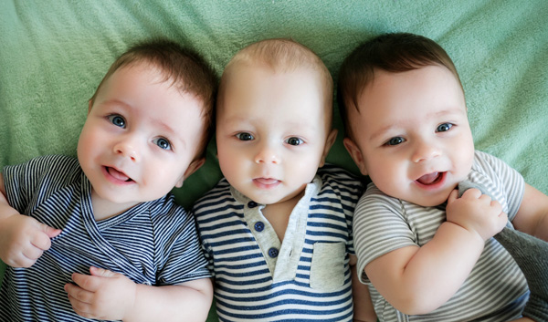 Photo of three infants and one is pulling their sock.