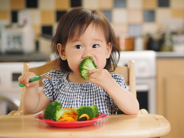 Photo of a young child eating brocoli.