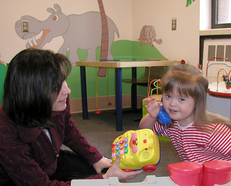 Photo of a young girl with Down Syndrome holding a phone and meeting with a clinician at an IHDD Specialty Clinic.