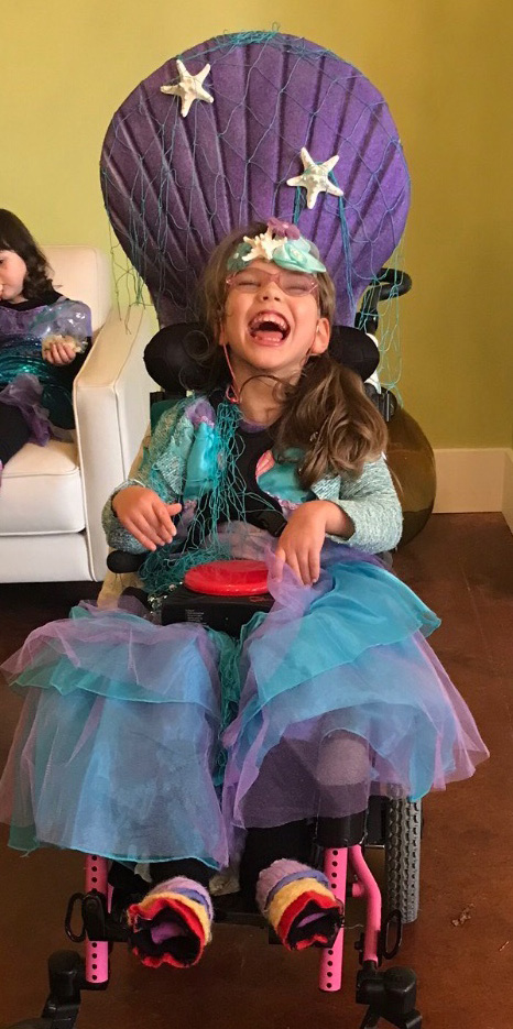 Photo of a young girl in a wheelchair dressed in bright colors and laughing.