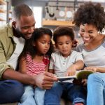 Photo of a family of four smiling and looking at a book together.
