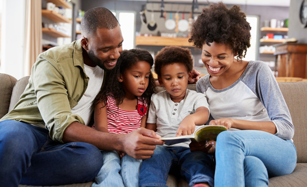 Photo of a family of four smiling and looking at a book together.