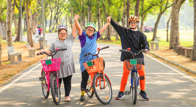 Photo of three bicycle riding friends holding and raising their hands on a park trail.