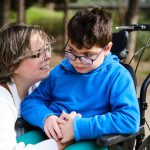 Photo of young child in a wheelchair with a smiling parent.