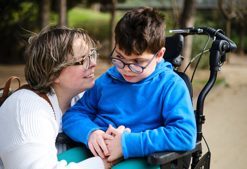 Photo of young child in a wheelchair with a smiling parent. 