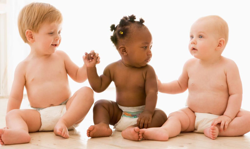 Photo: Three infants wearing diapers sitting on a floor.