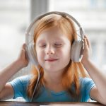 Photo: Young girl with her eyes closed wearing over the ears headphones.