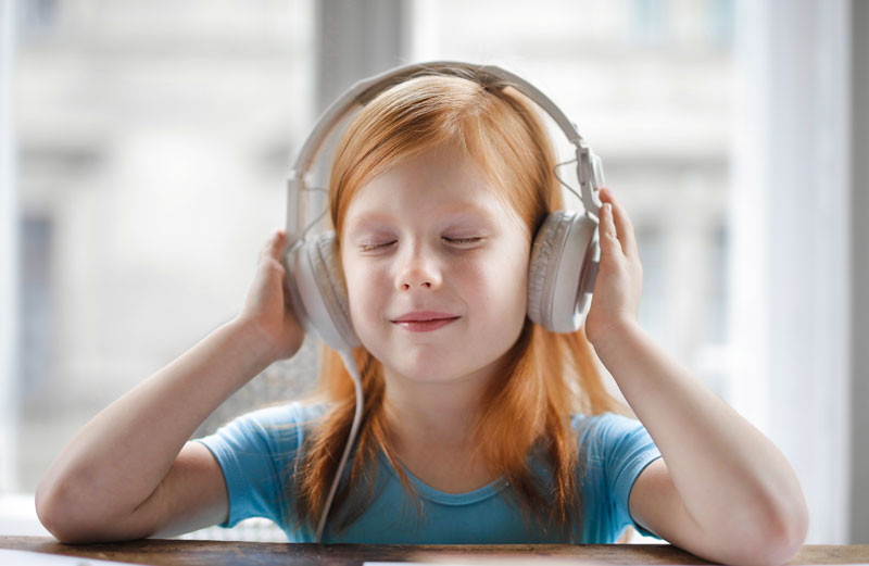 Photo: Young girl with her eyes closed wearing over the ears headphones. 