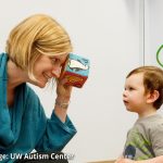 Photo: UW Autism Center Director Annette Estes looking through a block at a young child in a clinic setting.