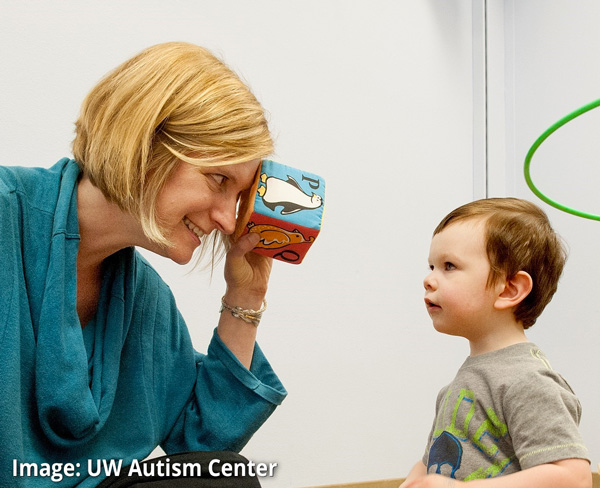 Photo: UW Autism Center Director Annette Estes looking through a block at a young child in a clinic setting.