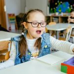 Photo: Excited girl with down syndrome sitting at desk smiling and playing in class.