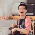 Photo: Smiling young man wearing an apron and in a wheelchair assisting with meal prep in a kitchen.