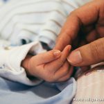 Photo: An adult hand holding the hand of a newborn infant. Photo by Aditya Romansa via Unsplash