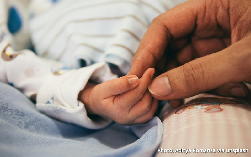Photo: An adult hand holding the hand of a newborn infant. Photo by Aditya Romansa via Unsplash