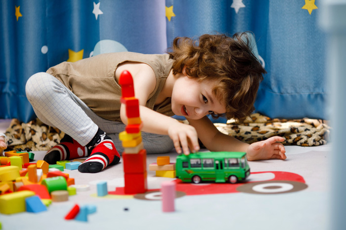 Photo: A young child playing with a toy bus on a play mat. 