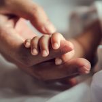 Photo: Parent holding an infant's hand.