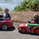 Photo: Two young children riding on mobility ride-on cars in the sunshine.