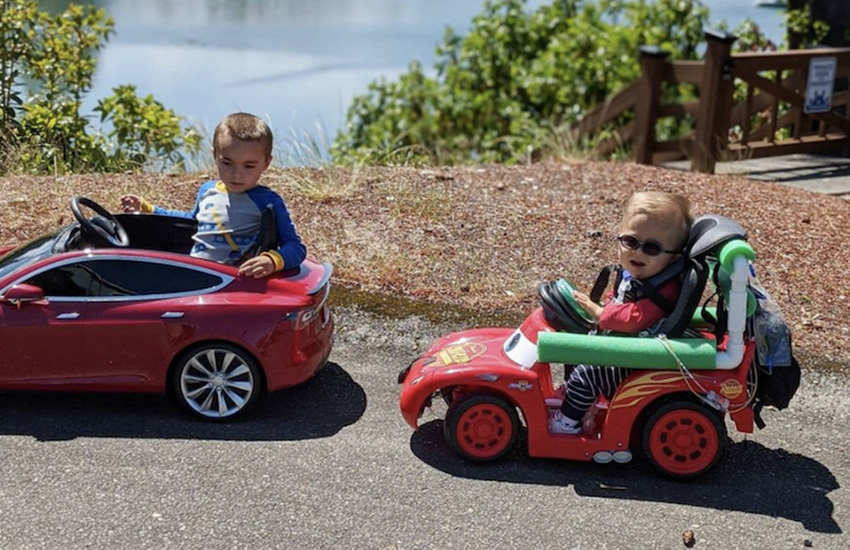 Photo: Two young children riding on mobility ride-on cars in the sunshine.