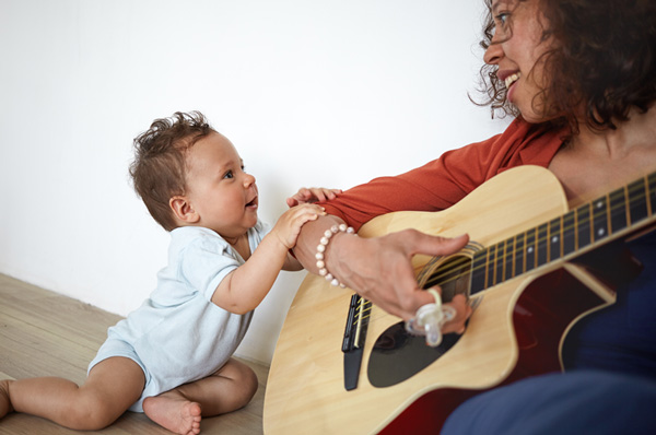 Photo: Infant smiling and holding onto mom while she plays the guitar.