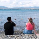 Photo: Young couple sitting on the beach together and looking at the water.