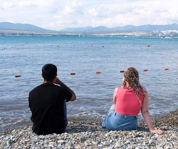 Photo: Young couple sitting on the beach together and looking at the water.