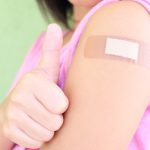 Photo of a child, wearing a bandage and holding their thumb up after receiving a vaccination shot.