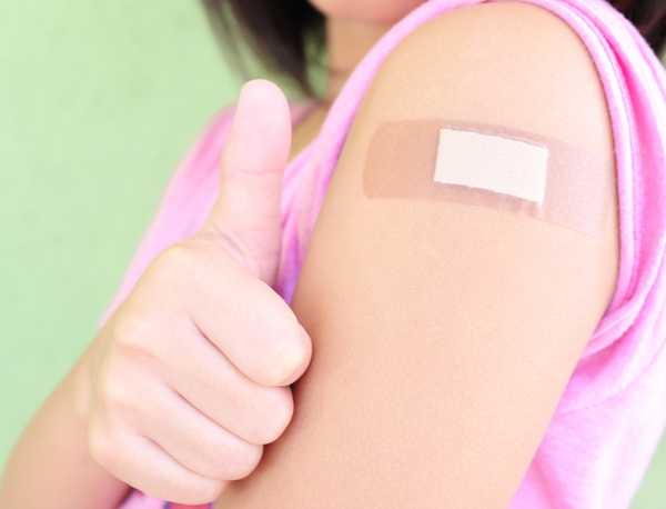 Photo of a child, wearing a bandage and holding their thumb up after receiving a vaccination shot. 