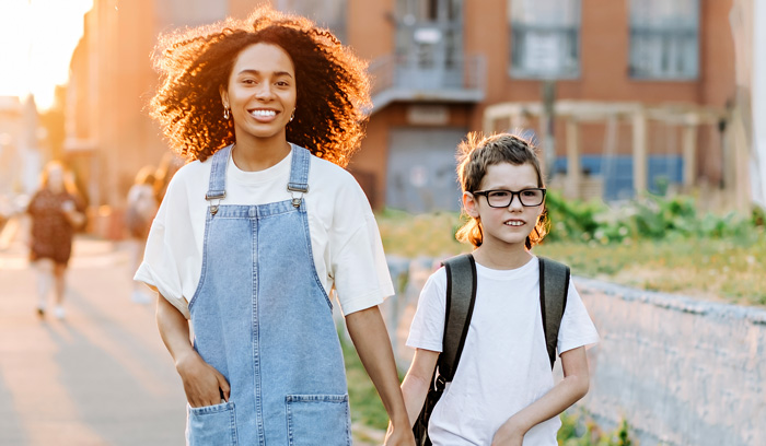 Photo: Two students holding hands, smiling, and walking to school. 