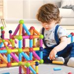 Toddler playing with ball and stick connector toys on the floor.