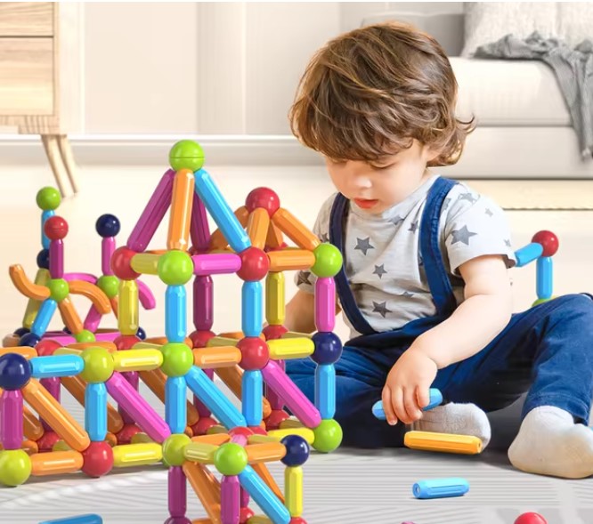 Toddler playing with ball and stick connector toys on the floor.