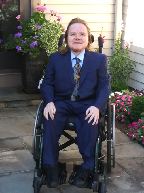 Photo: Carl James Dunlap sitting in his wheelchair, wearing a blue suit and smiling. 