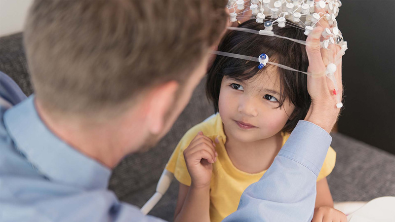 Photo: Researcher putting on a EEG Sensor Net on a young child's head for brain imaging. 