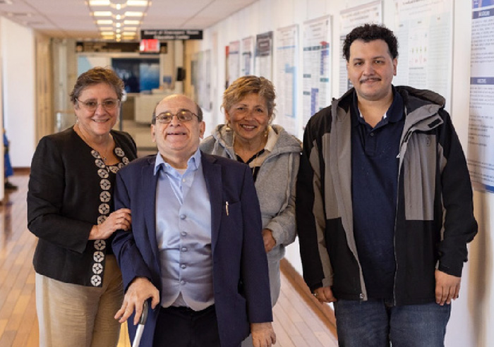 Photo: Four people standing and smiling in a hallway. One person has a cane.