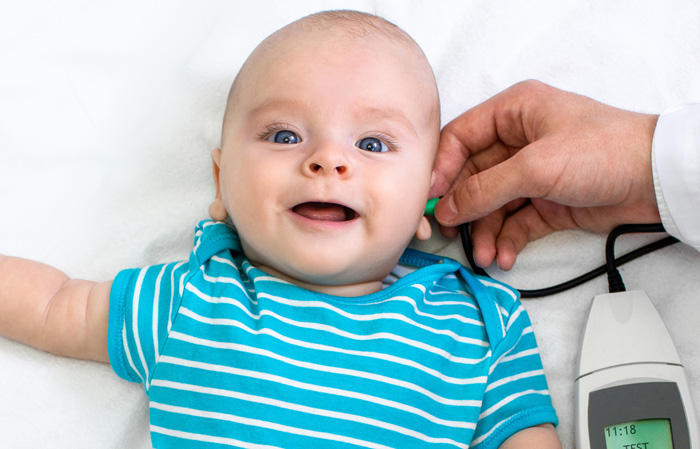 Photo of a doctor performing a hearing test on a smiling infant.