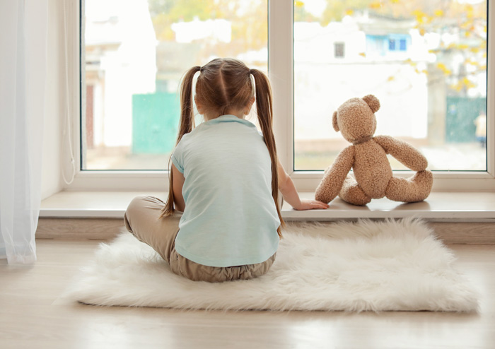 Photo: Young child with stuffed bear looking out a window together.
