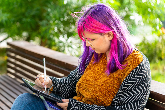 Photo: Young adult drawing while sitting on a park bench.