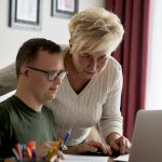 Mother and son with down syndrome working on a laptop together.