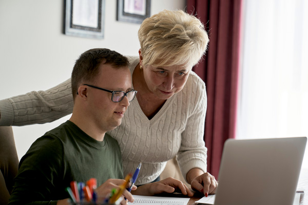 Mother and son with down syndrome working on a laptop together.