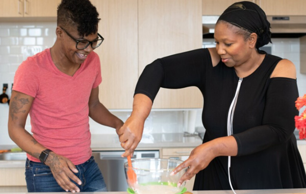 Adult child and parent smiling while preparing a meal.