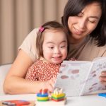 Young child with Down Syndrome smiling looking at a book.