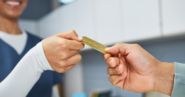 Smiling person handing a credit card to another person.
