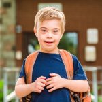 School age child with Down Syndrome wearing a backpack.