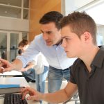 Summer intern working on a computer with a coach.