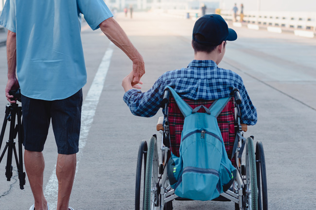 Man and adult child in wheelchair holding hands.