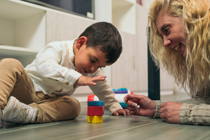 Mother smiling as her son stacks blocks.