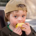 Young child wearing a baseball cap eating an apple.