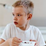 Young child with hearing aid eating a bowl of cereal.