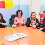 A teacher guides students with mental disabilities, including Down Syndrome, in sewing.