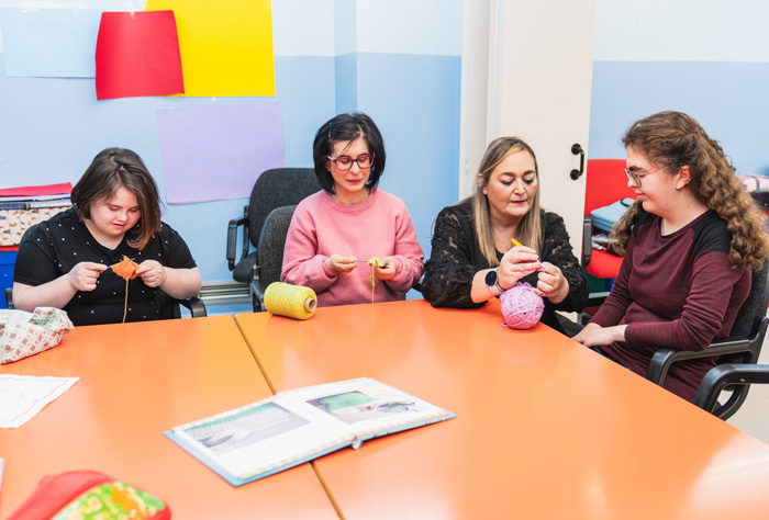 A teacher guides students with mental disabilities, including Down Syndrome, in sewing.