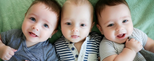 Photo of three infants and one is pulling their sock.